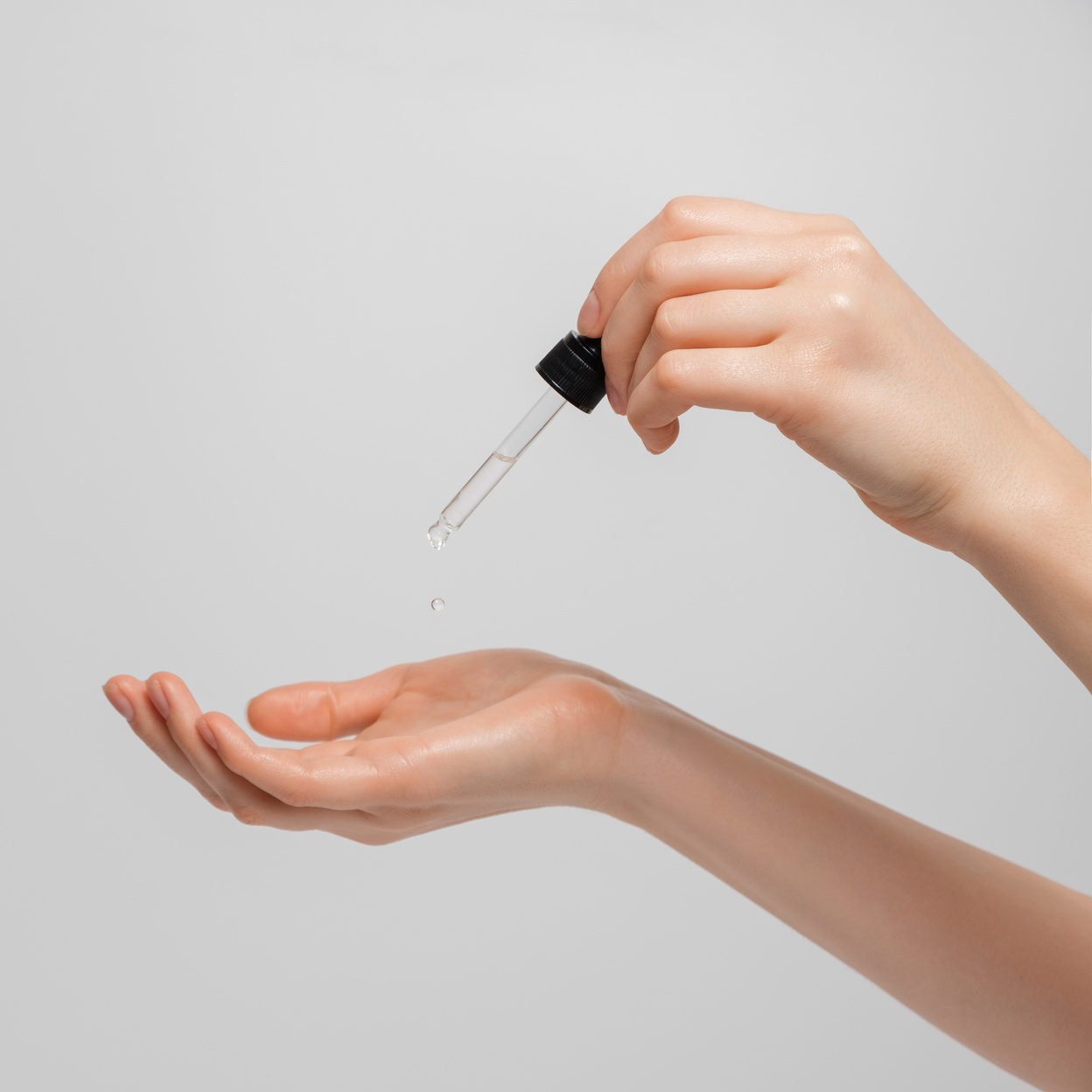Hand of woman with pipette drop of serum or hyaluronic acid on gray background. Hands of a beautiful woman dripping serum collagen.